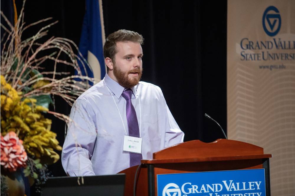 Man stands at a GVSU podium, wearing a nametag around his neck
